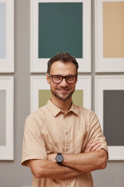 Foto retrato de jovem designer moderno em óculos em pé com os braços cruzados e sorrindo para a câmera