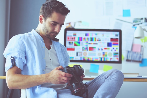 Retrato de jovem designer sentado no estúdio gráfico em frente ao laptop e computador enquanto trabalhava online