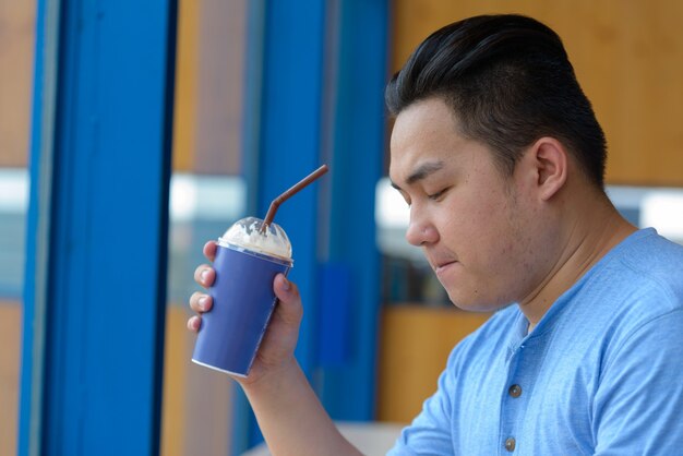 Retrato de jovem e bonito filipino com excesso de peso relaxando em uma cafeteria