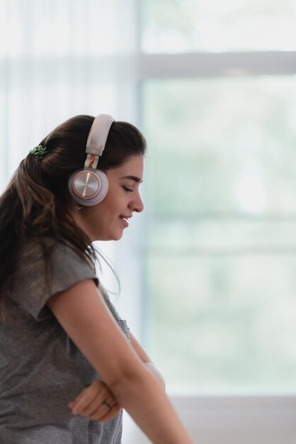 Retrato de jovem e despreocupado em roupas casuais, ouvindo música usando fones de ouvido bluetooth sem fio dançando e curtindo em casa com os olhos fechados