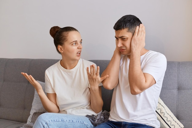 Retrato de jovem e homem brigando sentado no sofá e gritando esposa frustrada gritando masculino cobrindo olhos problema de relacionamento crise familiar