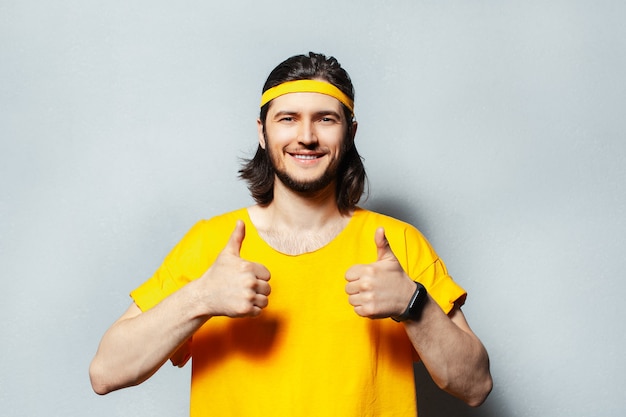 Retrato de jovem em camisa amarela aparecendo os polegares.