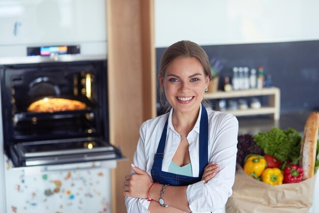 Retrato de jovem em pé com os braços cruzados contra o fundo da cozinha