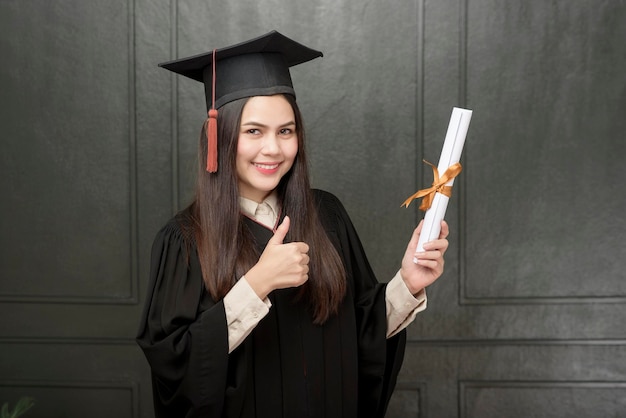 Retrato de jovem em vestido de formatura sorrindo e torcendo em fundo preto