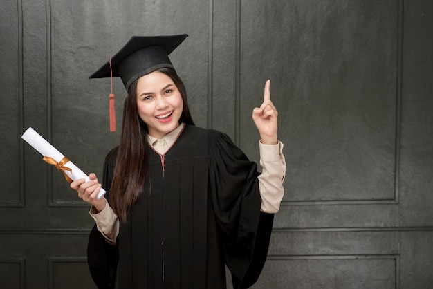 Retrato de jovem em vestido de formatura sorrindo e torcendo em fundo preto