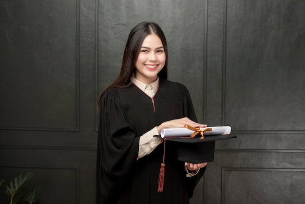 Retrato de jovem em vestido de formatura sorrindo e torcendo em fundo preto