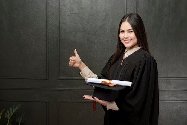 Retrato de jovem em vestido de formatura sorrindo e torcendo em fundo preto