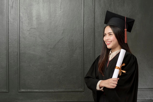 Retrato de jovem em vestido de formatura sorrindo e torcendo em fundo preto