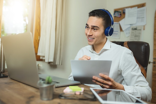 Foto retrato de jovem em videochamada com laptop e fones de ouvido, segurando um papel e mostrando algo.