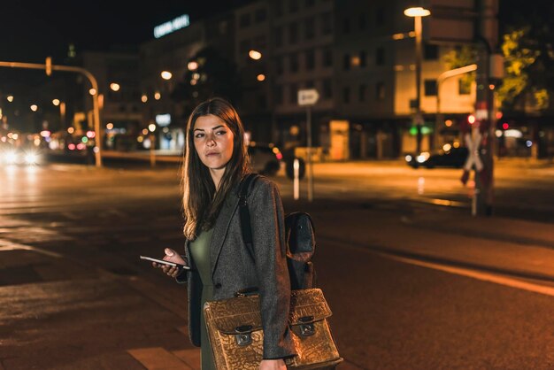 Foto retrato de jovem empresária com bagagem e celular à noite