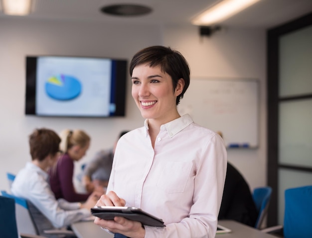 retrato de jovem empresária hispânica com computador tablet no interior do escritório de negócios de inicialização moderna, grupo de pessoas na reunião de equipe blured no fundo