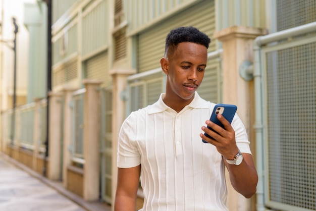 Retrato de jovem empresário africano confiante vestindo roupas casuais e usando telefone celular