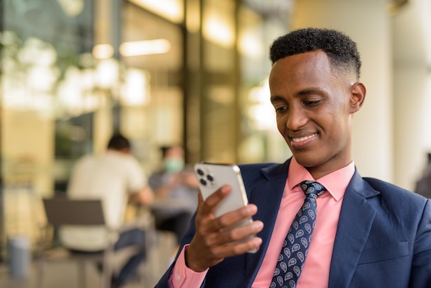 Retrato de jovem empresário africano de terno e gravata ao ar livre em uma cafeteria