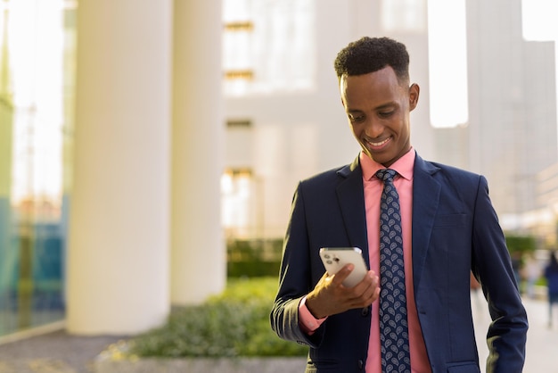 Retrato de jovem empresário africano de terno e gravata usando telefone celular