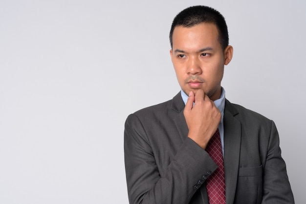 Retrato de jovem empresário asiático em terno com cabelo curto contra uma parede branca