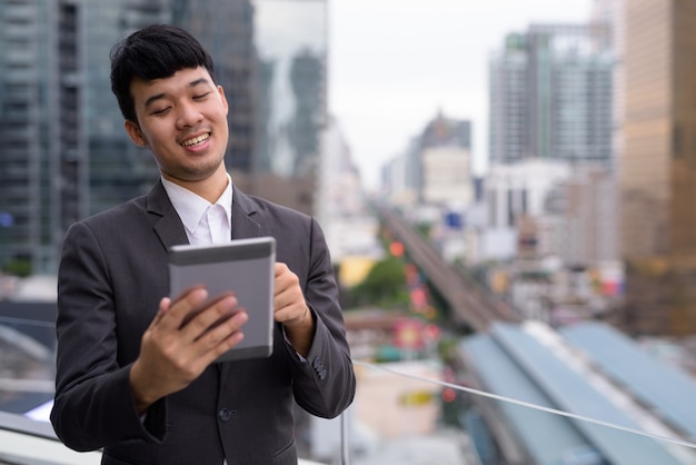 Retrato de jovem empresário asiático usando tablet digital contra a vista da cidade