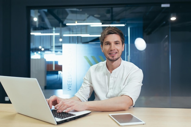 Retrato de jovem empresário com homem de barba trabalhando em escritório moderno com laptop sorrindo e olhando para a câmera