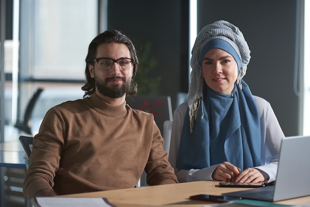 Retrato de jovem empresário e empresária muçulmana em hijab, olhando para a câmera enquanto trabalha no escritório