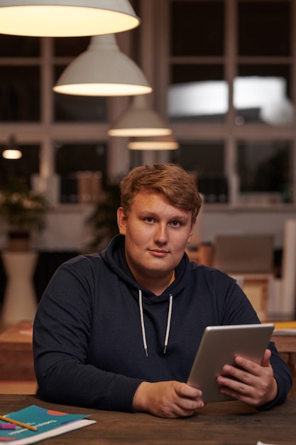 Retrato de jovem empresário em roupas casuais, olhando para a frente enquanto trabalha em um tablet digital