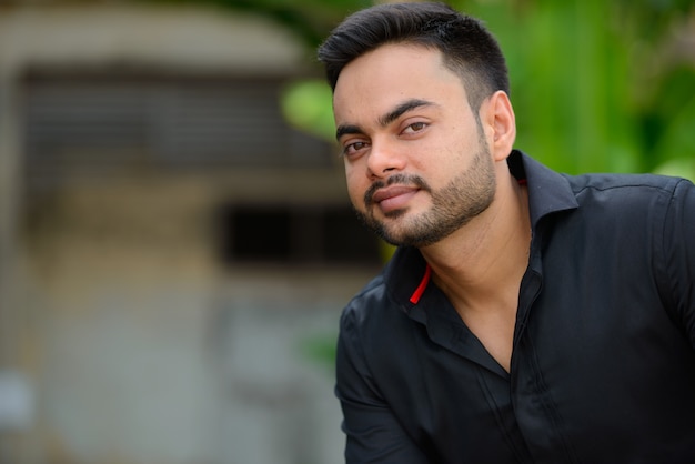 Retrato de jovem empresário indiano barbudo bonito na cidade ao ar livre