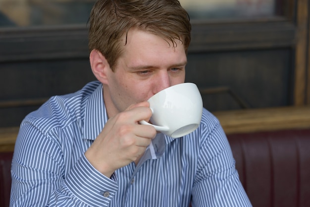 Retrato de jovem empresário loiro bonito relaxando em uma cafeteria ao ar livre