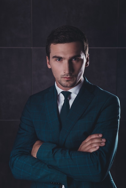 Retrato de jovem empresário sério em um terno preto com as mãos cruzadas