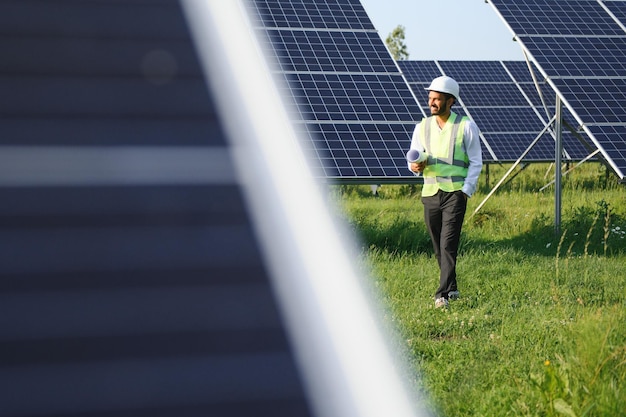 Retrato de jovem engenheiro indiano em pé perto de painéis solares com fundo de céu azul claro habilidade de energia renovável e limpa espaço de cópia da índia