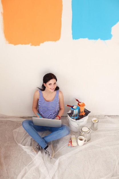 Retrato de jovem enquanto pinta novo apartamento sentado com laptop Jovem mulher com laptop