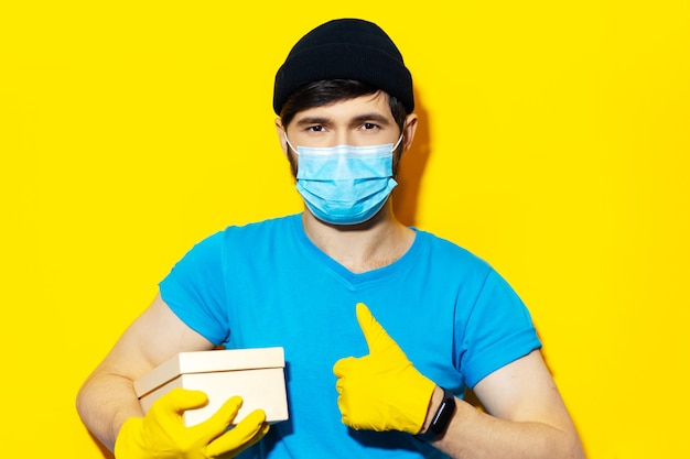 Retrato de jovem entregador de camisa azul, usando máscara médica e luvas amarelas