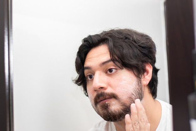 Retrato de jovem espalhando creme de barbear na barba do espelho com espaço para cópia