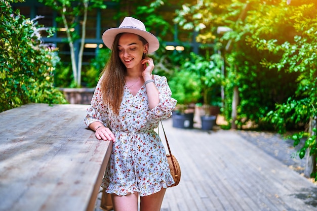 Retrato de jovem feliz alegre sorridente linda linda morena jovem com cabelo comprido, usando chapéu e macacão curto no café verde em dia ensolarado de verão