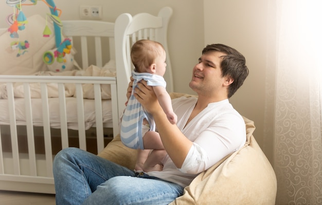 Retrato de jovem feliz brincando com seu bebê no quarto