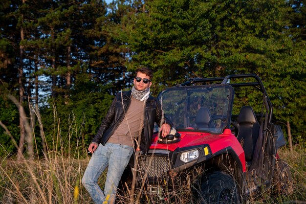 retrato de jovem feliz desfrutando de um lindo dia ensolarado fumando um cigarro enquanto faz uma pausa de dirigir um carro de buggy off road na natureza montanhosa