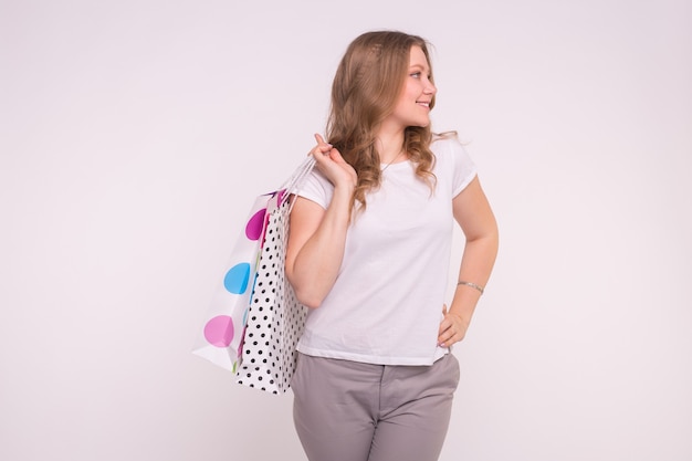 Retrato de jovem feliz e sorridente com sacolas de compras na parede branca