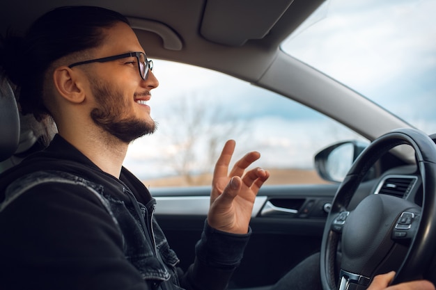 Foto retrato de jovem feliz, explicando algo e dirigindo o carro