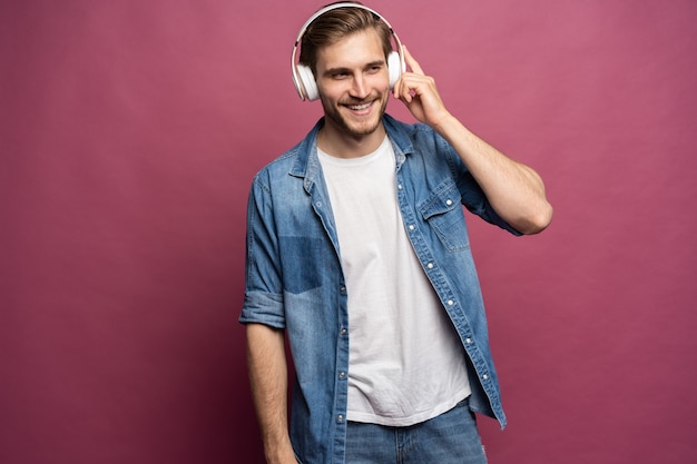 Retrato de jovem feliz ouvindo música com fones de ouvido isolados sobre fundo rosa.