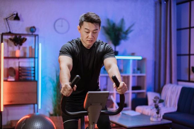 Retrato de jovem focado vestindo roupas esportivas usando bicicleta ergométrica