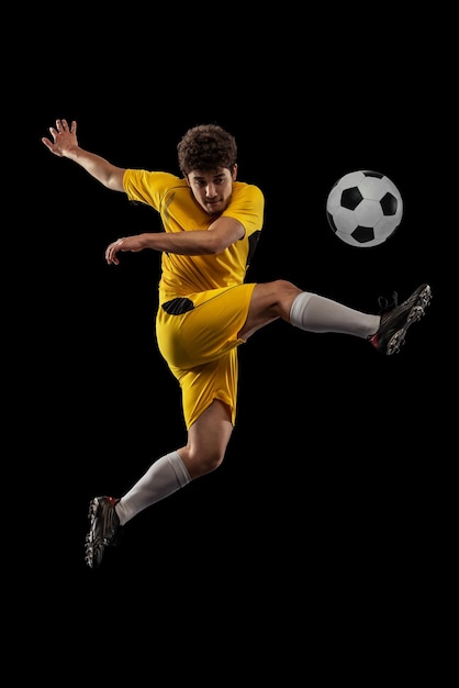 Retrato de jovem futebol jogando em treinamento de movimento isolado sobre fundo de estúdio preto Chutando bola