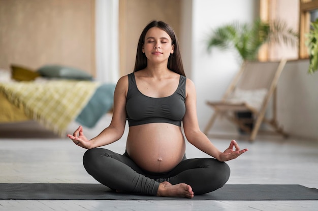 Retrato de jovem grávida meditando no tapete de ioga em casa