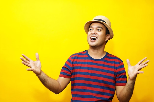 Retrato de jovem hipster jovem feliz vestido casual camiseta listrada vermelha e usar chapéus Gesto de emoção estender os braços tímido modesto em retratos de estúdio definir cor de fundo amarelo