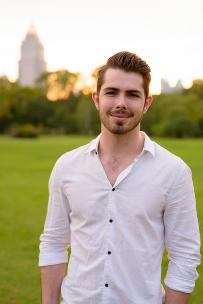 Retrato de jovem homem barbudo bonito relaxante no parque ao ar livre