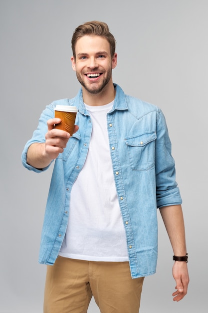 Retrato de jovem homem bonito caucasiano em camisa jeans segurando uma xícara de café para viagem