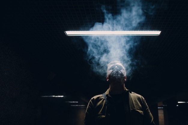 Retrato de jovem homem caucasiano fumando cigarro no escuro com luz de linha.