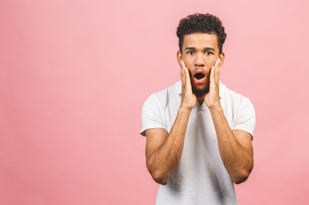 Retrato de jovem homem espantado com penteado afro em branco t-shir, olhando na câmera com a boca aberta e expressão chocada.