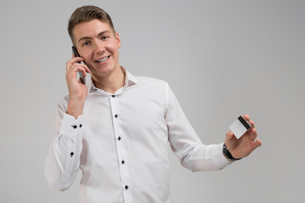 Retrato de jovem homem falando no celular com cartão de crédito na mão isolado no branco