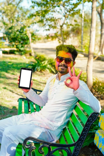 Retrato de jovem indiano feliz no festival de cores holi usando telefone celular