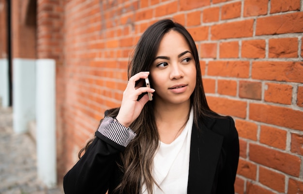 Retrato de jovem latina falando ao telefone, ao ar livre na rua.