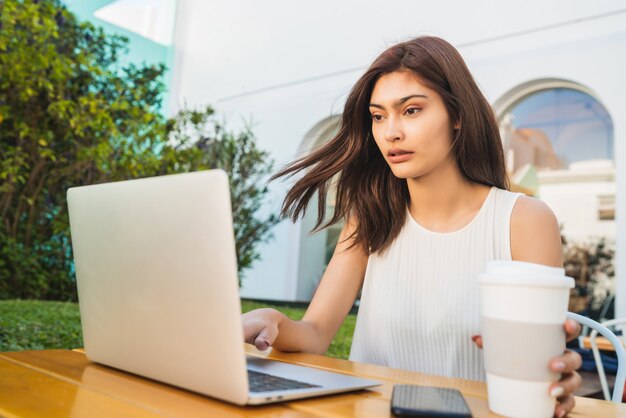 Retrato de jovem latina usando seu laptop enquanto está sentado em uma cafeteria. Conceito de tecnologia e estilo de vida.