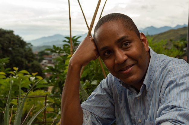 Retrato de jovem latino-americano com sentimentos de expressão facial de emoção positiva, segurando a cabeça com uma mão com a natureza em segundo plano