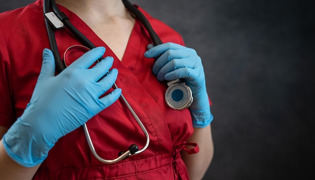 Retrato de jovem médica enfermeira em luvas de casaco vermelho e chapéu com estetoscópio isolado no escuro Conceito de saúde médica